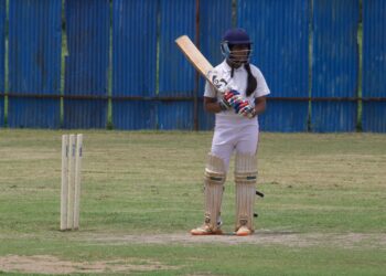 Female cricketer preparing to bat on a grass field (Pexels 13509971)