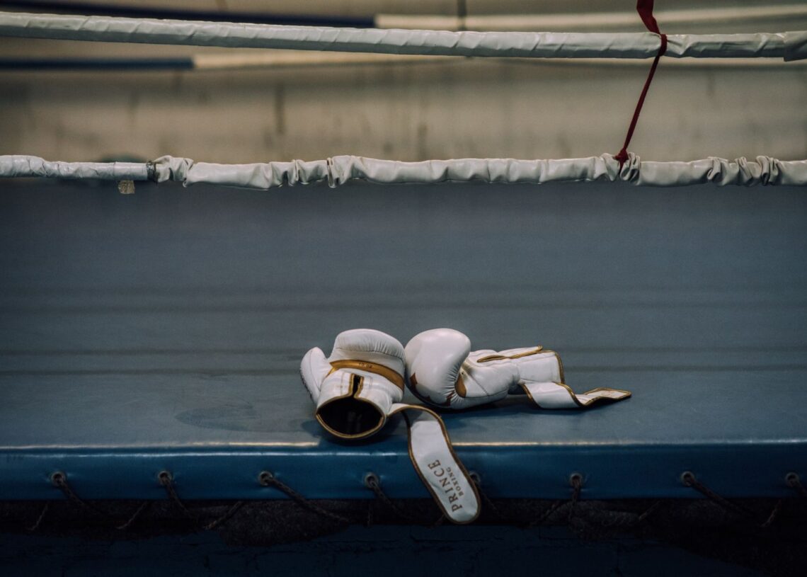 White boxing gloves resting on the canvas of an empty ring (Pexels 9944239)