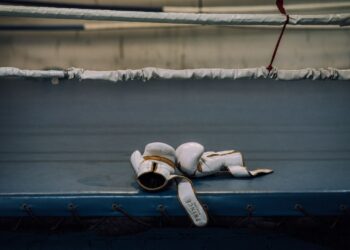 White boxing gloves resting on the canvas of an empty ring (Pexels 9944239)